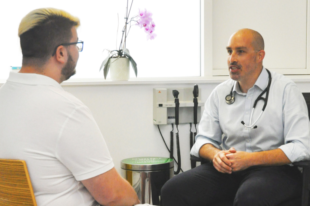 a man sitting in a chair talking to another man.