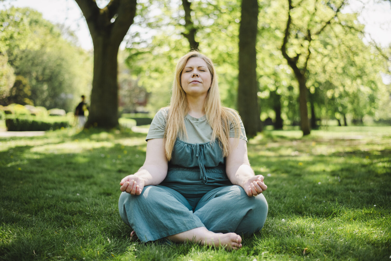 Person with long blonde hair meditating sitting on green grass - Image provided courtesy of Leeds Beckett University - leedsbeckett.ac.uk