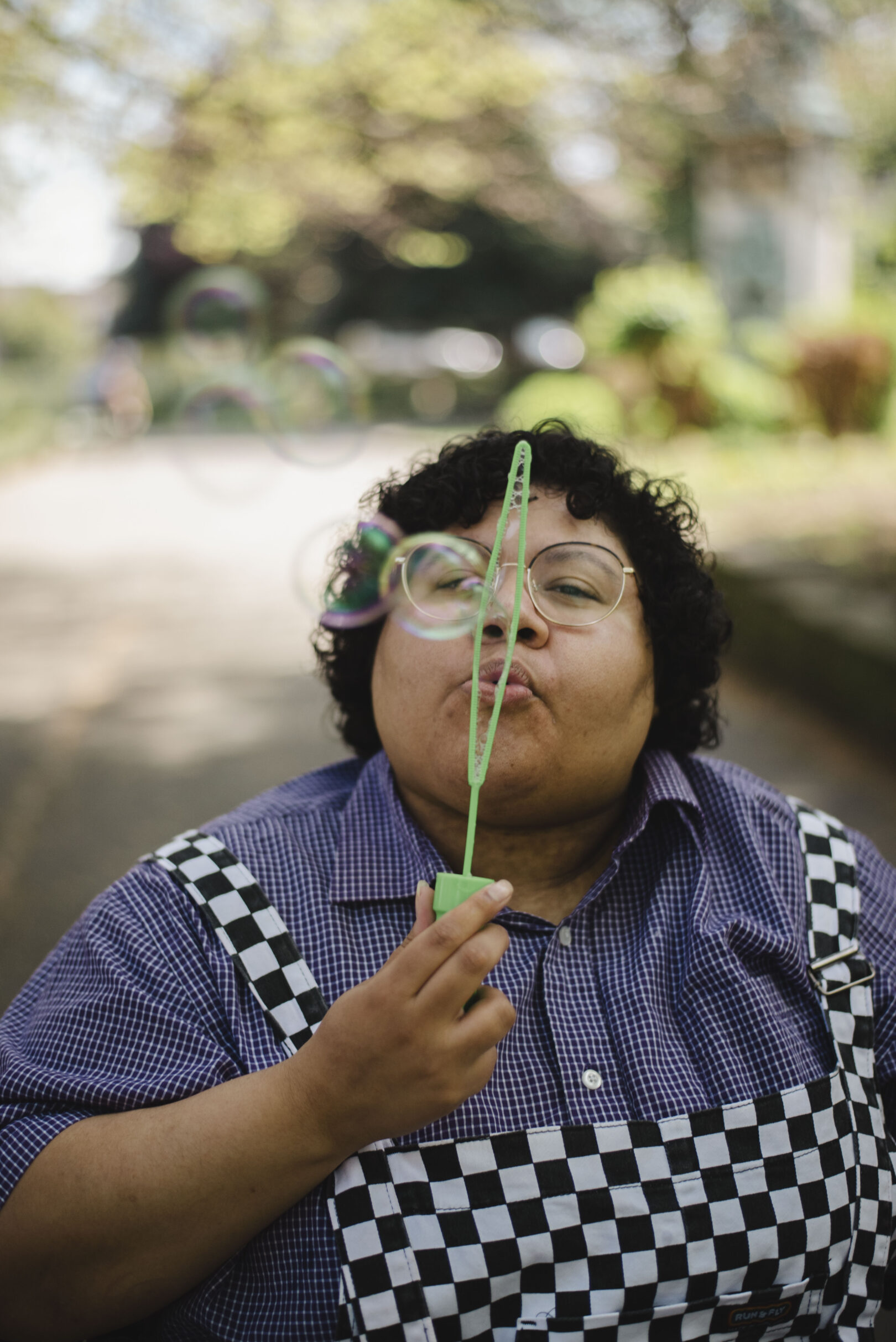 A person wearing glasses and a checkered dress blows bubbles outdoors on a sunny day. Image provided courtesy of Leeds Beckett University - leedsbeckett.ac.uk